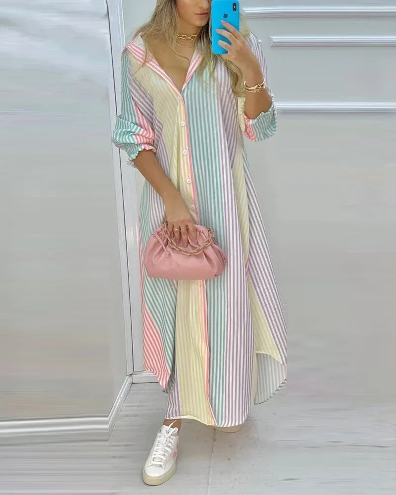 Woman wearing a long sleeve button-down shirt dress with pastel vertical stripes, holding a pink clutch and white sneakers.